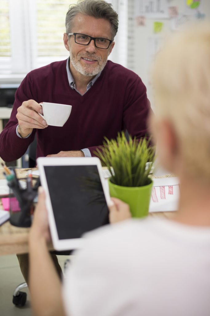 man drinking coffee and listening to his secretary